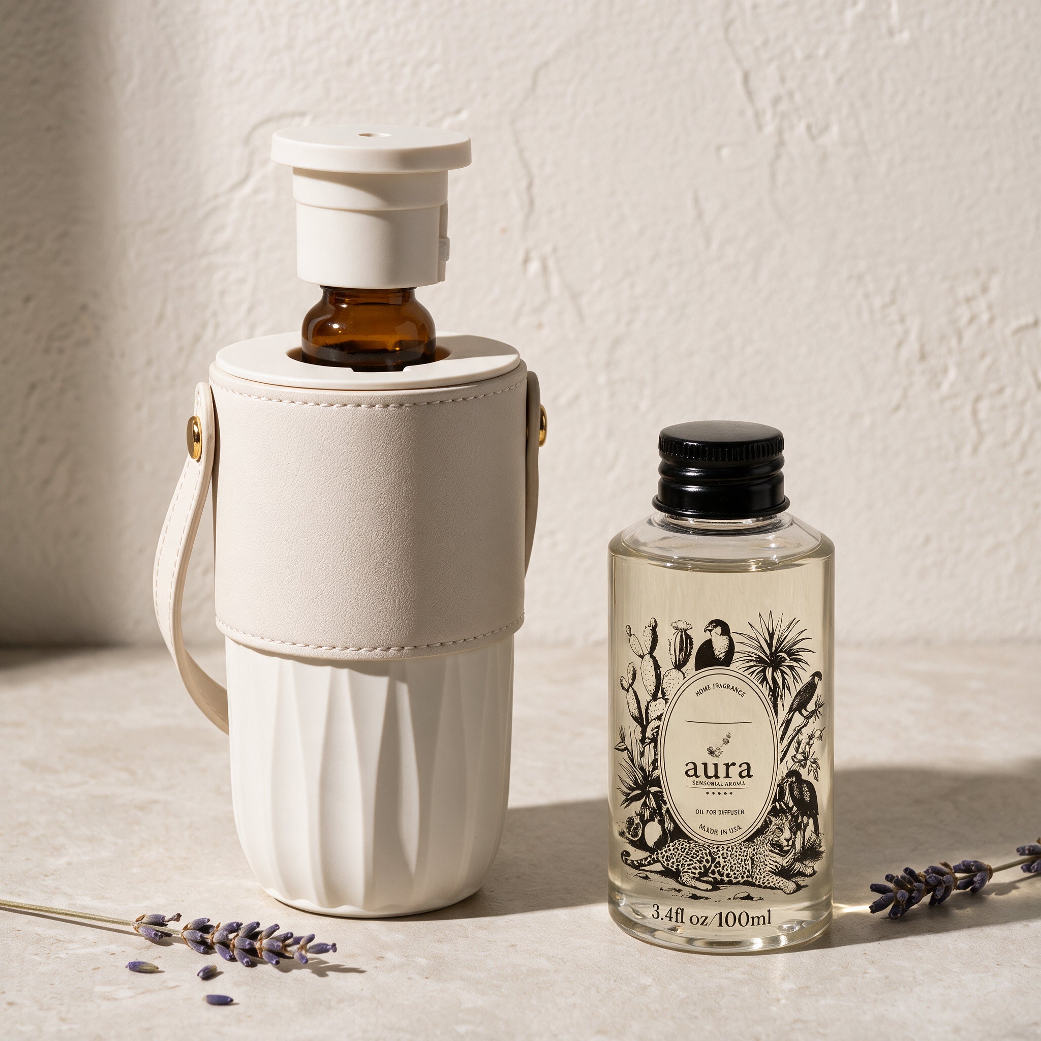 AURA Nomade diffuser open with the amber oil vial inserted, beside the AURA 100 ml fragrance oil